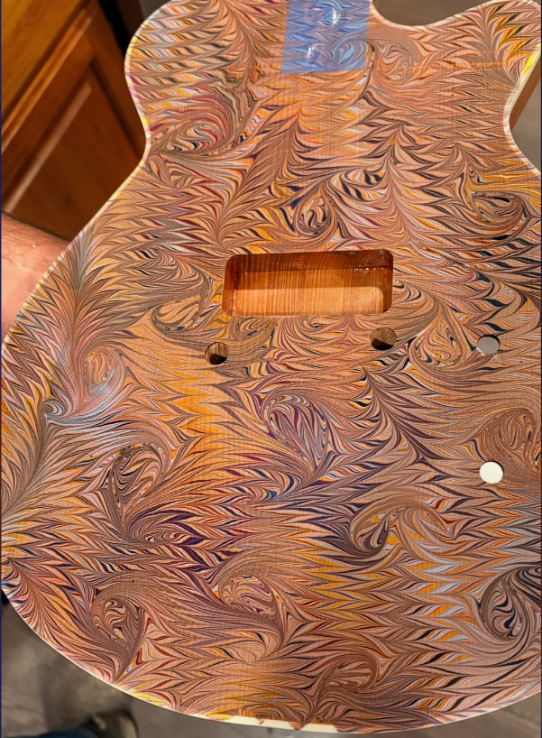The second body, marbled in copper, plum, and blue, the wood grain showing through.